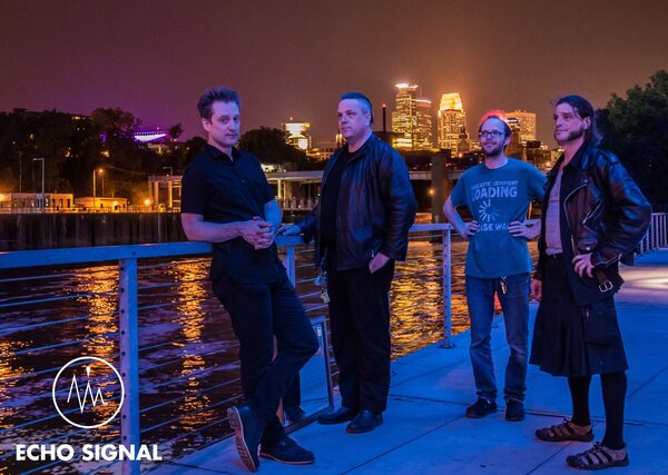 Adam, John, Charles, and Phaedrus (Echo Signal in 2016) on the riverfront with the Minneapolis skyline behind them.