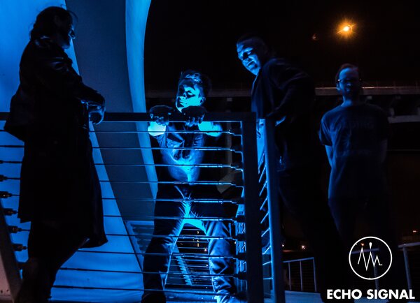 Night photo of Phaedrus, Adam, John, and Charles (Echo Signal in 2016) on the blue-lit Lowry Avenue bridge over the Mississipi.