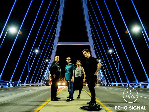John, Charles, Phaedrus, and Adam (Echo Signal in 2016) standing together in the middle of the empty Lowry Ave bridge at night, the blue-lit cables of a bridge converging overhead.